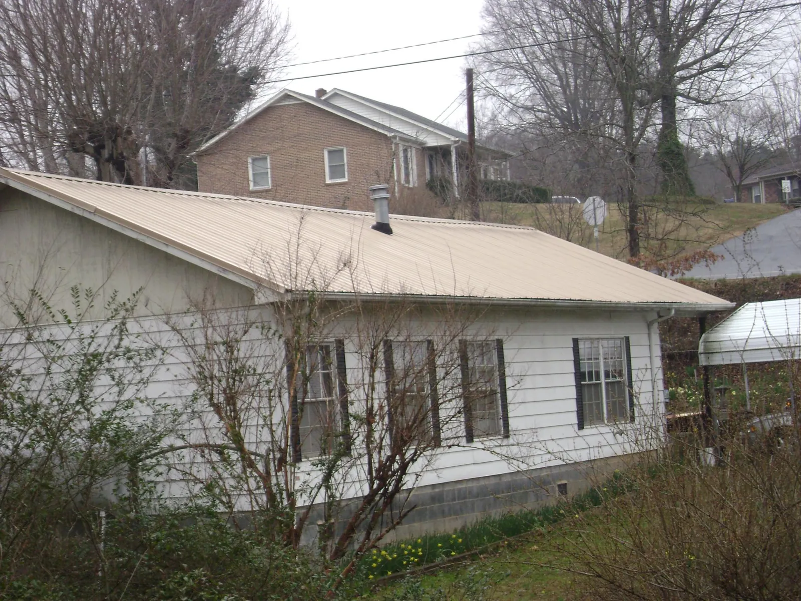 Tan metal roof on a white sided house set into a hillside — Commercial Roofing by Roofing Brothers in Middleburg